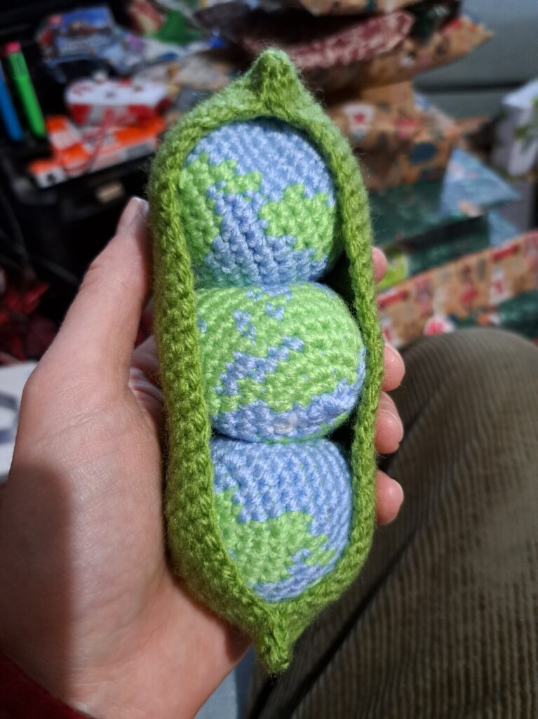 Three crocheted planet Earths in a crocheted pea pod.