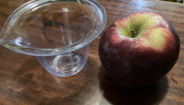 One Cortland apple next to a 1 cup measuring cup.